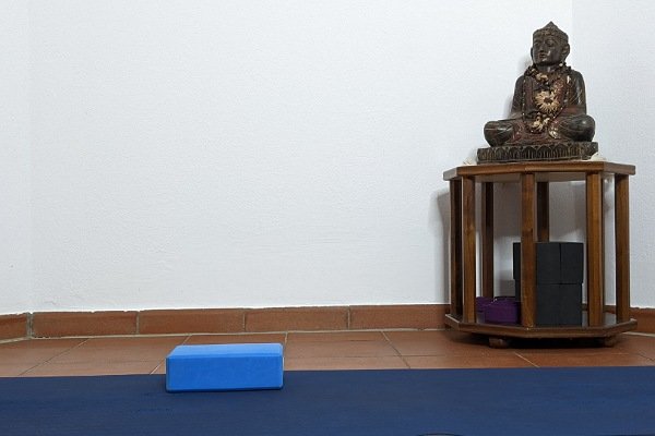 Yogamatte, Yogablock und Buddhastatue auf Tischchen